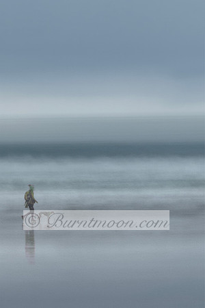 A minimalist photograph with a muted blue-grey palette, showing a lone person walking a thin dog, possibly a sighthound, on a wet, reflective beach. The horizon and waves are blurred into soft, horizo