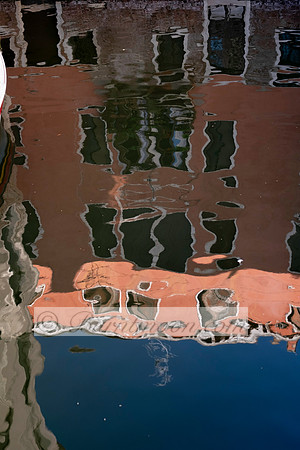 A distorted reflection of a Venetian building in a canal, with terracotta, green, and blue tones rippling across the water's surface.