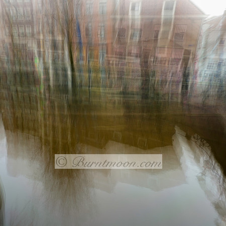 Abstract ICM photograph of Amsterdam canal houses reflected in water, with soft, vertical motion blur creating a dreamlike effect.