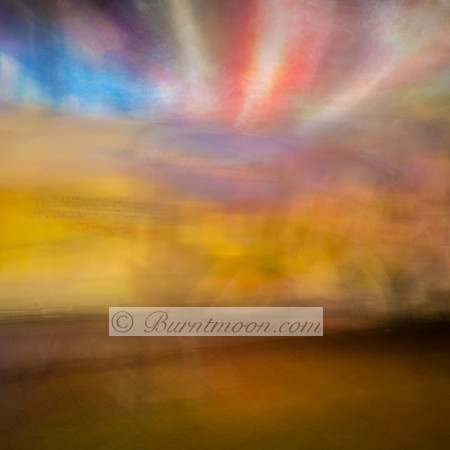 Abstract urban photograph with blurred motion, featuring warm yellow tones, bursts of red and blue light, and a soft, dreamlike texture.
