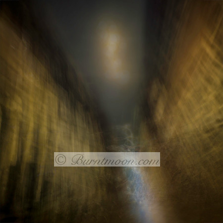Abstract night scene of an alley in Amsterdam with blurred golden buildings and a glowing light in the center, created using intentional camera movement.