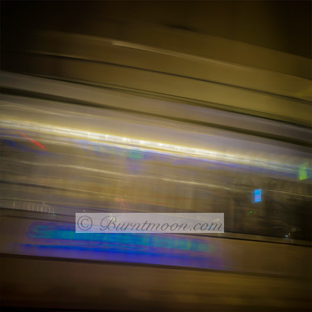 A blurred photograph of a moving tram in Amsterdam at night, with streaks of blue and gold light creating an abstract sense of speed and motion.
