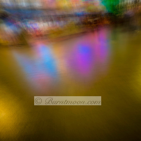 Abstract ICM photograph of colorful reflections on a golden surface, featuring blurred pink, blue, and green hues in a surreal urban setting.